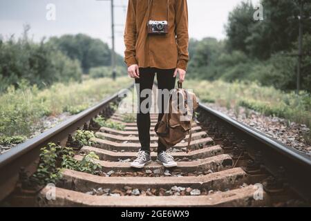 Photographe en veste marron avec sac à dos et appareil photo rétro sur chemin de fer Banque D'Images