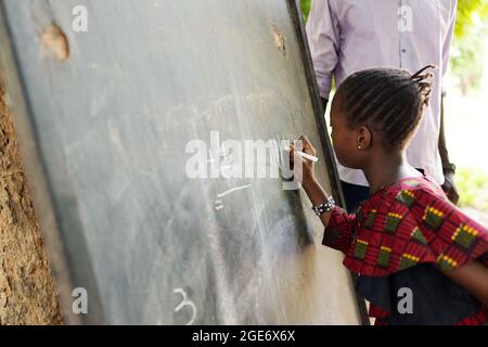 Vue rapprochée d'une petite écolière africaine noire qui écrit des points de tally sur un tableau noir avec une grosse craie Banque D'Images
