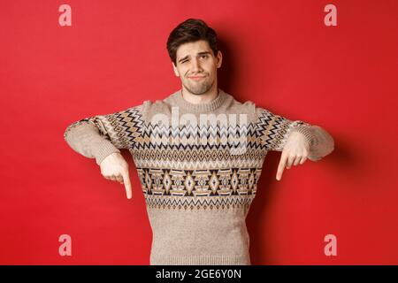 Concept de fête de noël, de vacances d'hiver et de style de vie. Homme doué et méfiant, montrant quelque chose de mauvais, pointant les doigts vers le bas et Banque D'Images