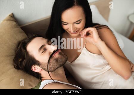 bonne femme regardant l'homme faisant la moustache de ses cheveux de brunette dans le lit Banque D'Images