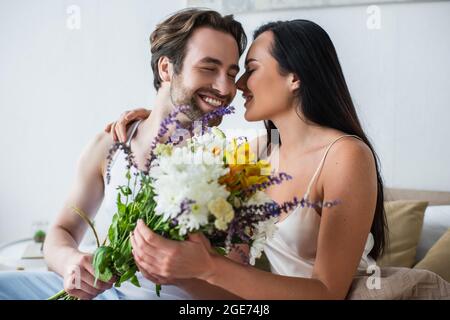 joyeux homme donnant un bouquet de fleurs à une petite amie souriante dans la chambre Banque D'Images