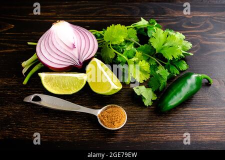 Herbes et épices utilisées pour assaisonner les haricots et le riz : oignon rouge, coriandre, piment jalapeno, quartiers de lime et cumin sur une table en bois Banque D'Images