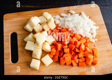 Pommes de terre hachées, carottes et oignon sur une planche à découper : oignon pelé et coupé en dés avec tomates hachées et carottes sur une planche à découper Banque D'Images