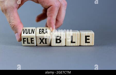 Symbole vulnérable ou flexible. Homme d'affaires transforme les cubes en bois et les mots « vulnérable » en « flexible ». Magnifique arrière-plan gris, espace de copie. Bus Banque D'Images