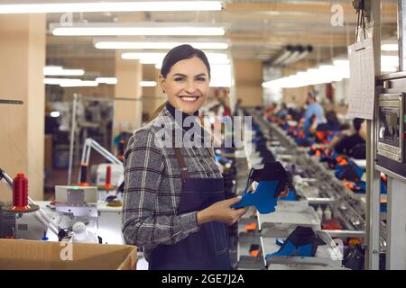 Souriante femme créateur de chaussures souriant à l'appareil photo tenant une partie de nouvelles chaussures Banque D'Images