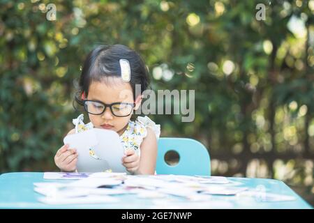 Adorable petite fille portant des lunettes joue avec des cartes éducatives en plein air Banque D'Images