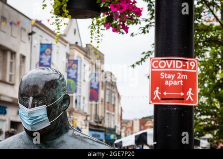 « The Sockman », de l'artiste écossais Shona Kinloch, représente l'industrie de la bonneterie de Loughborough et est vu ici avec un masque facial à côté d'un panneau Covid Banque D'Images