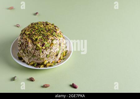 Prêt à manger de la halva de sésame avec des pistaches sur une assiette blanche et peu de noix éparses sur fond de papier vert. Bonbons traditionnels du Moyen-Orient. Juif, Banque D'Images