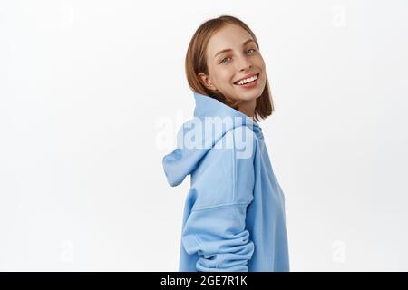 Portrait d'une jeune fille blonde belle, tournez son visage à la caméra avec un large sourire heureux, regardant avec les yeux bleus, debout dans des vêtements décontractés contre Banque D'Images