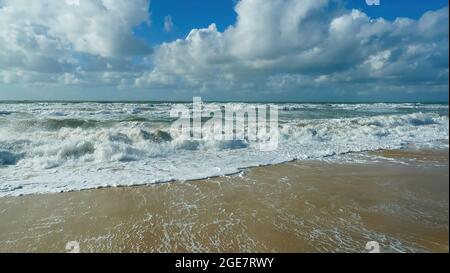 Vue sur la plage de sable sur les vagues dans l'océan atlantique français contre les nuages au ciel bleu - Soulac-sur-mer, Bretagne, France Banque D'Images