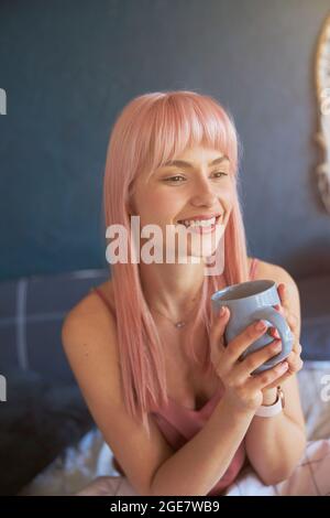 Le joli mannequin féminin peut contenir une tasse de boisson délicieuse sur le lit Banque D'Images
