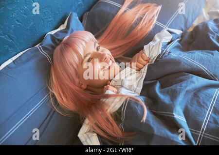 Le modèle positif de la femme avec des cheveux rose vif se trouve dans un grand lit tôt le matin Banque D'Images