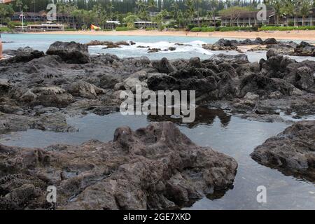 Des bassins de marée se sont formés sur des roches volcaniques bordant la plage de sable des touristes de la baie de Napili sur la plage et dans l'eau à Maui, Hawaï Banque D'Images