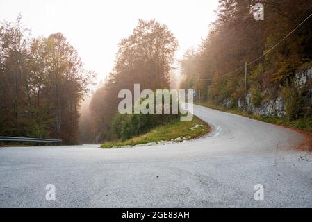 Virage en épingle à cheveux le long d'une route alpine brumeuse au coucher du soleil en automne Banque D'Images