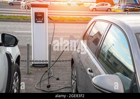 Une voiture électrique est chargée à la station de charge dans un parking extérieur le long d'une rue dans un centre-ville Banque D'Images