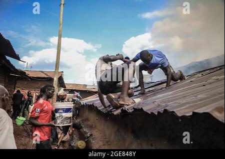 Nairobi, Kenya. 17 août 2021. Des jeunes de la région grimpent sur les toits pour aider à faire feu à Bombolulu, Kibera.les résidents se sont joints aux mains pour aider à faire feu, qui s'est produit aujourd'hui après-midi à partir de fils électriques emmêlés alimentant différentes maisons en électricité. Le feu a rasé douze maisons et propriétés laissant la plupart des résidents bloqués. Crédit : SOPA Images Limited/Alamy Live News Banque D'Images