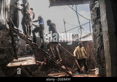 Nairobi, Kenya. 17 août 2021. Les résidents grimpent sur le toit pour aider à mettre un feu à Bombolulu, Kibera.les résidents se sont joints aux mains pour aider à mettre un feu qui s'est produit aujourd'hui après-midi à partir de fils électriques enchevêtrés fournissant l'alimentation à différentes maisons. Le feu a rasé douze maisons et propriétés laissant la plupart des résidents bloqués. Crédit : SOPA Images Limited/Alamy Live News Banque D'Images