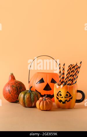 Halloween amusant décorations de fête, bol de bonbons, citrouilles, bonbons, mug avec paille de boisson sur fond orange. Composition verticale pour Halloween avec copie Banque D'Images