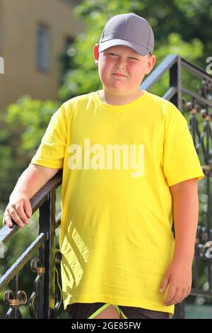 Un jeune garçon dans un T-shirt jaune et une casquette et des lunettes de soleil se tient dans la nature. Photo de haute qualité Banque D'Images