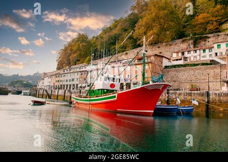 Bateau rouge qui se distingue du reste pour sa couleur rouge vif, dans le port, en arrière-plan il y a des arbres et un beau ciel bleu Banque D'Images