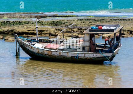 Camacari, Bahia, Brésil - 17 octobre 2015 : ancien bateau de pêche amarré derrière les rochers corail sur la plage de Camacari, Bahia. Banque D'Images