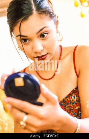 Une femme qui vérifie son maquillage et ses cheveux dans un miroir compact dans sa main. Banque D'Images