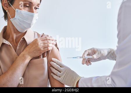 Femme d'âge moyen au visage masque médical qui reçoit l'injection du vaccin contre le coronavirus covid19 Banque D'Images