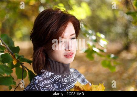 Portrait extérieur de la jeune femme caucasienne en chandail tricoté posé sur fond de nature. Une belle femme avec une expression pensive se repose dans le parc. Sur fond d'arbres Banque D'Images