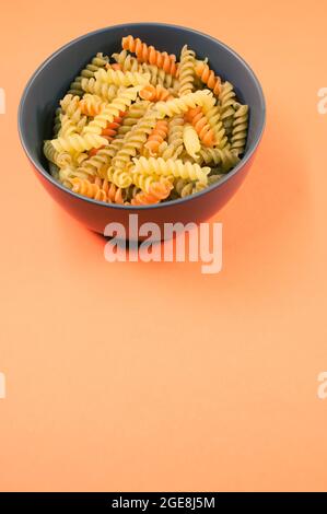 Plan vertical de pâtes rotini tricolores sur un bol isolé sur fond orange Banque D'Images