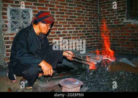 Un forgeron chauffe des morceaux de fer à forger dans un keris, une sorte de poignard traditionnel. Yogyakarta, Indonésie – 24 novembre 2009 Banque D'Images