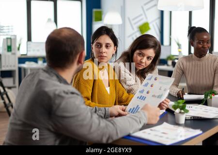 Des femmes occupées et multiculturelles analysent les statistiques financières annuelles sur le bureau, qui tiennent des documents à la recherche de solutions d'affaires. Équipe d'hommes d'affaires travaillant en entreprise, brainstorming Banque D'Images