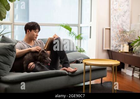 Jeune homme chinois avec chien de compagnie sur le canapé Banque D'Images
