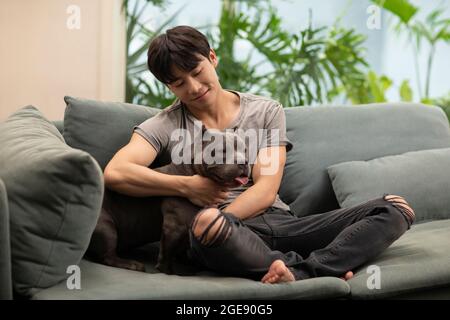 Jeune homme chinois avec chien de compagnie sur le canapé Banque D'Images