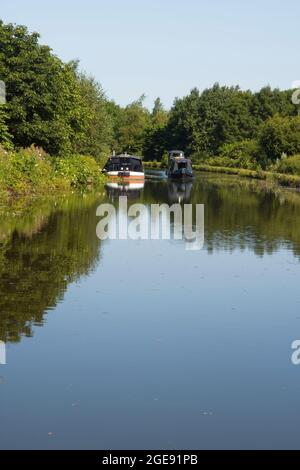 Un bateau à rames passe devant un bateau à faisceau de câblage amarré dans un virage près de Burscough sur le canal Leeds & Liverpool Banque D'Images