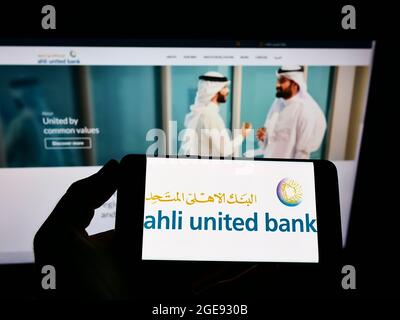 Personne tenant un téléphone portable avec le logo de la société bahreini Ahli United Bank (AUB) à l'écran en face de la page Web d'affaires. Mise au point sur l'affichage du téléphone. Banque D'Images