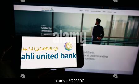 Personne tenant un smartphone avec le logo de la société bahraini Ahli United Bank (AUB) à l'écran devant le site Web. Mise au point sur l'affichage du téléphone. Banque D'Images