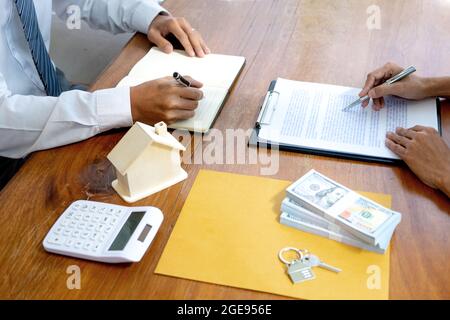 Les hommes d'affaires et les clients lisent et signent des contrats d'achat ou de location d'une maison ou d'un bien immobilier sur une table avec des documents et des modèles de maison. Banque D'Images