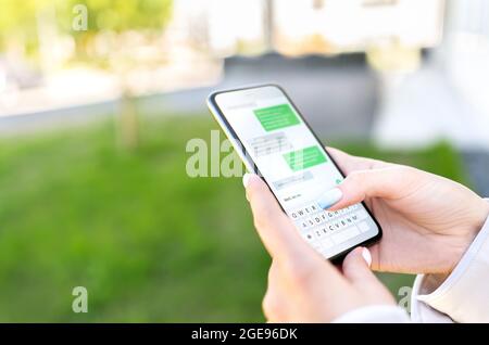SMS avec téléphone dans le parc extérieur de la ville. Femme envoyant un message texte avec un téléphone portable. Discussion sur l'application de messagerie instantanée. Personne utilisant un smartphone. Banque D'Images