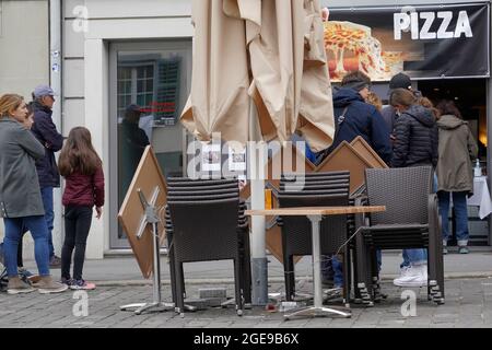 Restaurant pizza proposant uniquement des plats à emporter. Les chaises et les tables sont agrafées et hors service. Les clients font une file d'attente pour acheter un à emporter. Banque D'Images