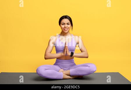 Concept de yoga du matin. Bonne dame afro-américaine pratiquant la méditation en position lotus, assise sur un tapis Banque D'Images