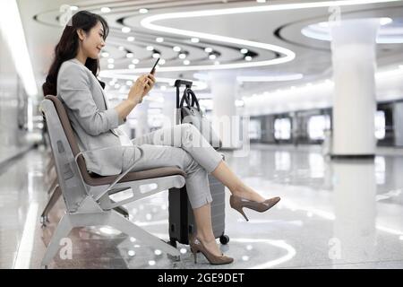 Jeune femme d'affaires chinoise utilisant un smartphone à l'aéroport Banque D'Images