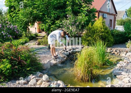 l'homme nettoie le fond de l'étang de jardin avec un nettoyeur haute pression de la boue et de la boue. Banque D'Images