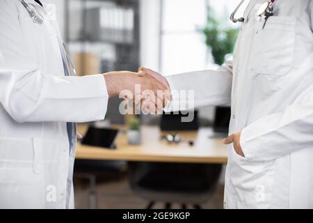 Medicaid, assurance, soins de santé, concept de médecine. Deux médecins masculins méconnaissables se secouent les mains, en gros plan. Vue floue de la table dans un bureau moderne en arrière-plan Banque D'Images