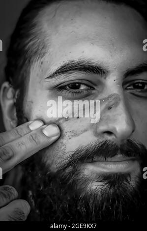 Portrait noir et blanc serré d'un homme barbu du Moyen-Orient mettant de la boue sur son visage Banque D'Images