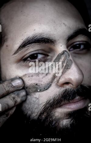 Portrait serré d'un homme barbu du Moyen-Orient mettant de la boue sur son visage Banque D'Images