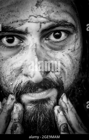 Portrait noir et blanc serré d'un homme barbu du Moyen-Orient mettant de la boue sur son visage Banque D'Images