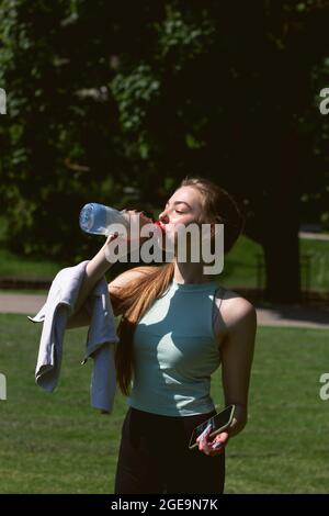 La jeune femme caucasienne en vêtements de sport est de boire de l'eau après l'entraînement. Fitness en plein air Banque D'Images