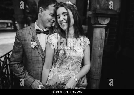 Élégante mariée heureuse et marié souriant et embrassant sur fond de vieille église. Mariage provençal. Beau couple de mariage émotionnel riant et câlin Banque D'Images