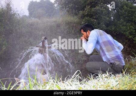 Équipement agricole pour l'irrigation de champ, un agriculteur indien buvant de l'eau de jet d'eau débordant sur sa ferme, brouillard de pluie, concentration sélective Banque D'Images