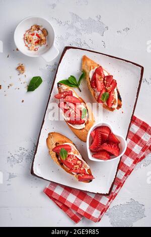 Sandwichs ouverts avec fraises, fromage doux à la menthe et aux noix dans une assiette en céramique sur fond de pierre gris clair. Nourriture estivale et saine, légumes Banque D'Images